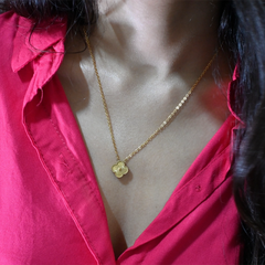 Gold necklace with a flower pendant worn by a person in a red shirt.